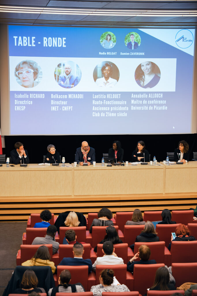 Photo d'une table ronde avec 6 personnes sur une estrade et une assemblée
