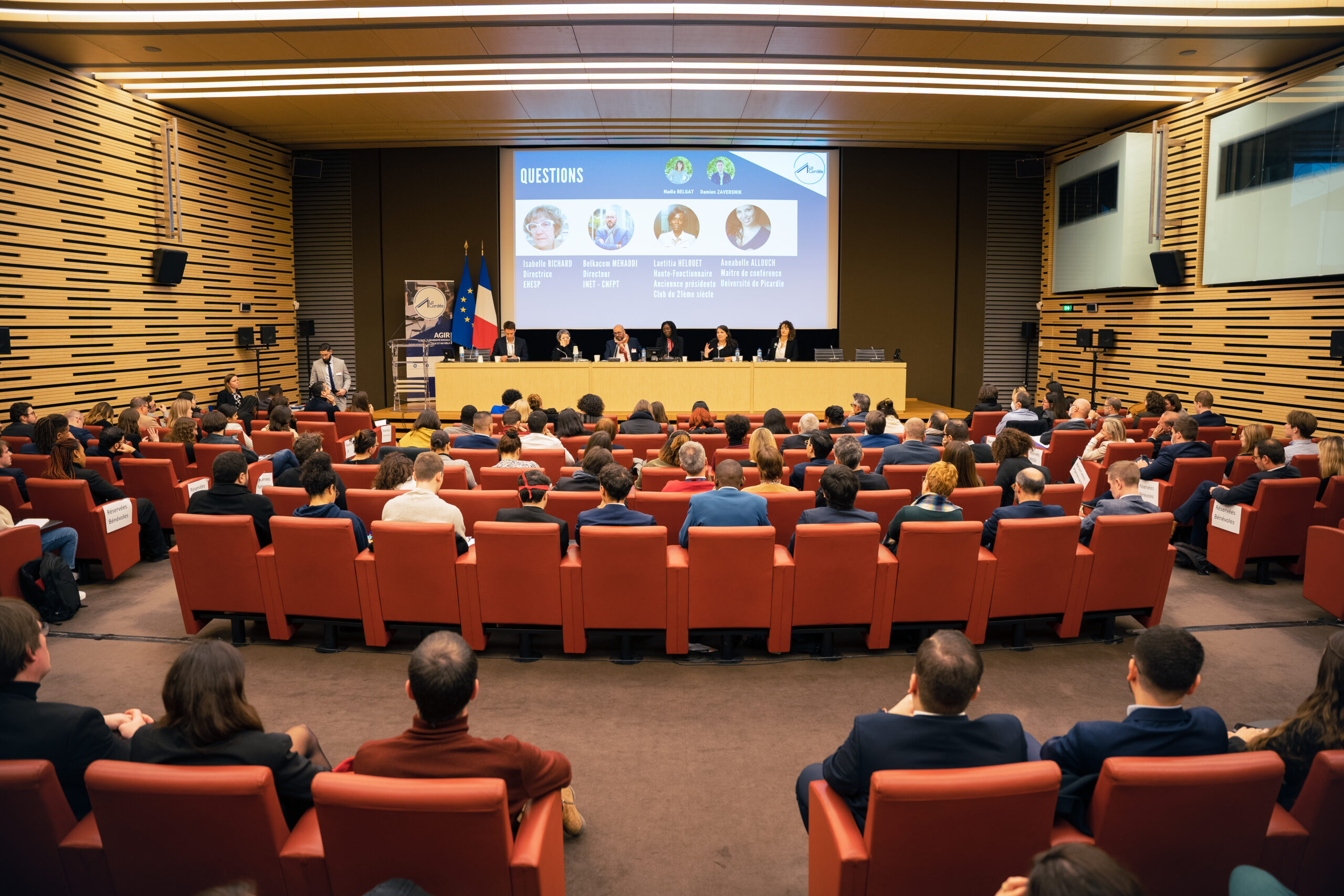 Photo d'une table ronde avec 6 personnes sur une estrade et une assemblée